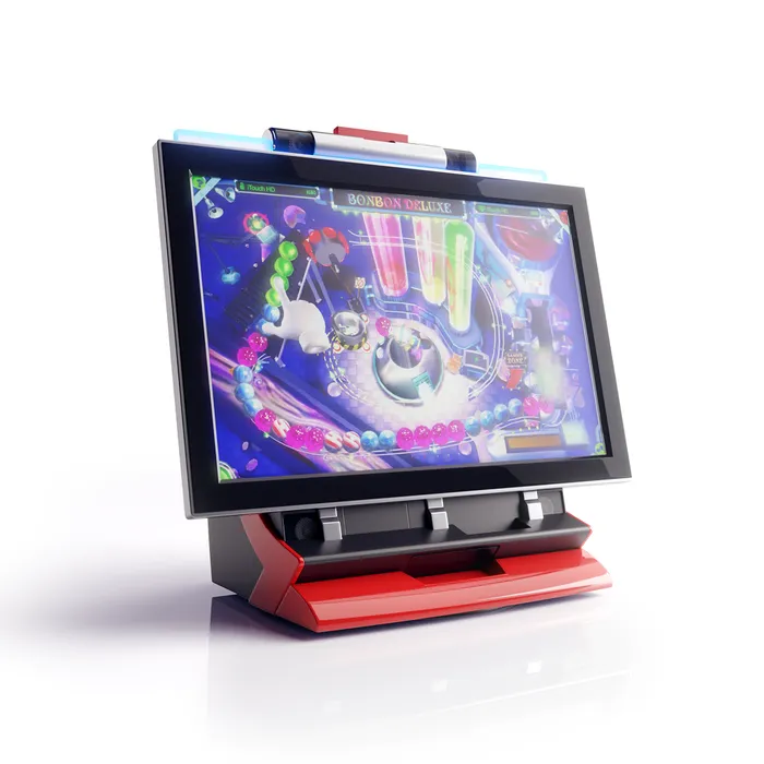 A touchscreen arcade machine with a wide screen showing a colourful game, above a red and black base