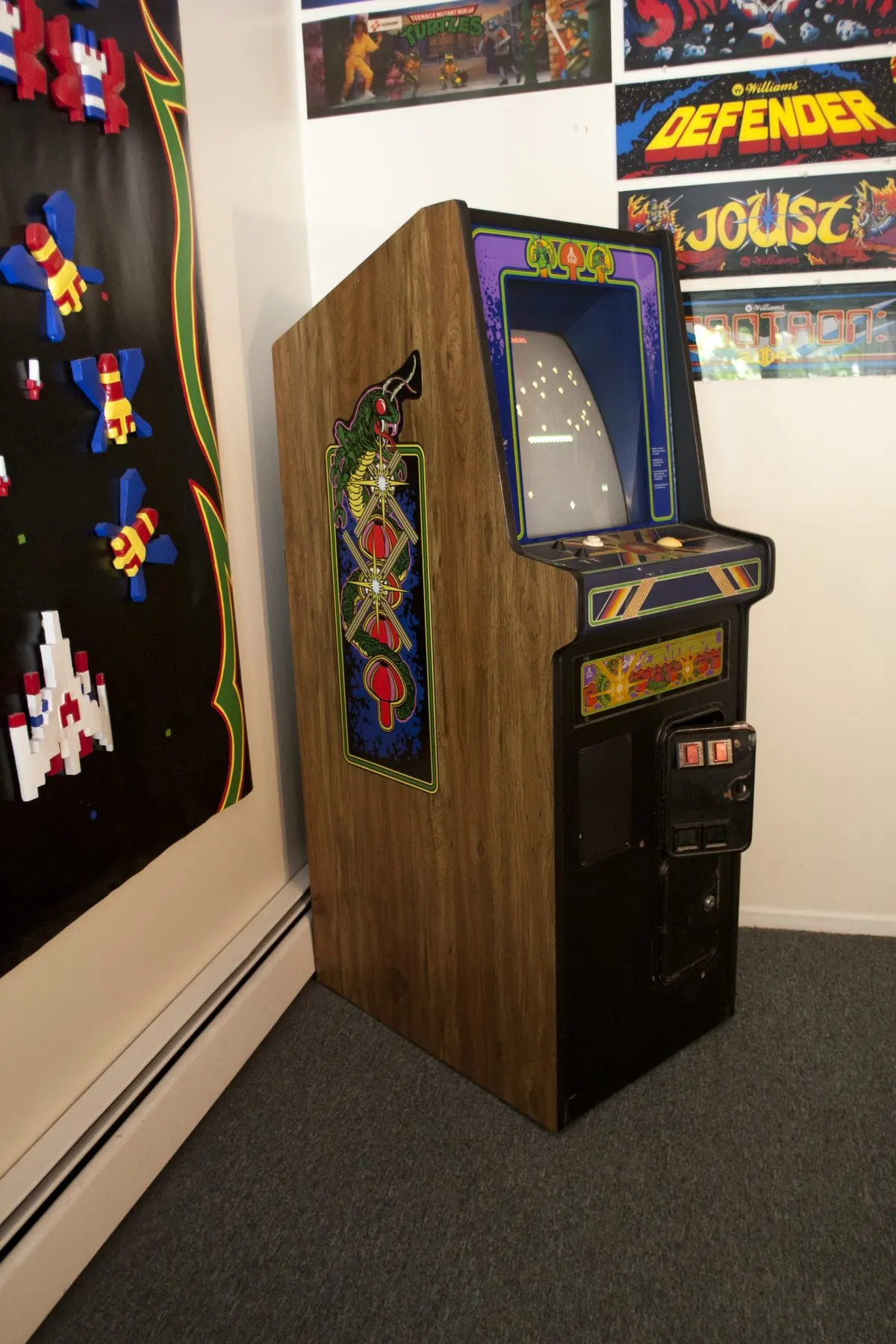 A restored 1981 cabaret arcade cabinet in a home game room next to framed arcade marquees