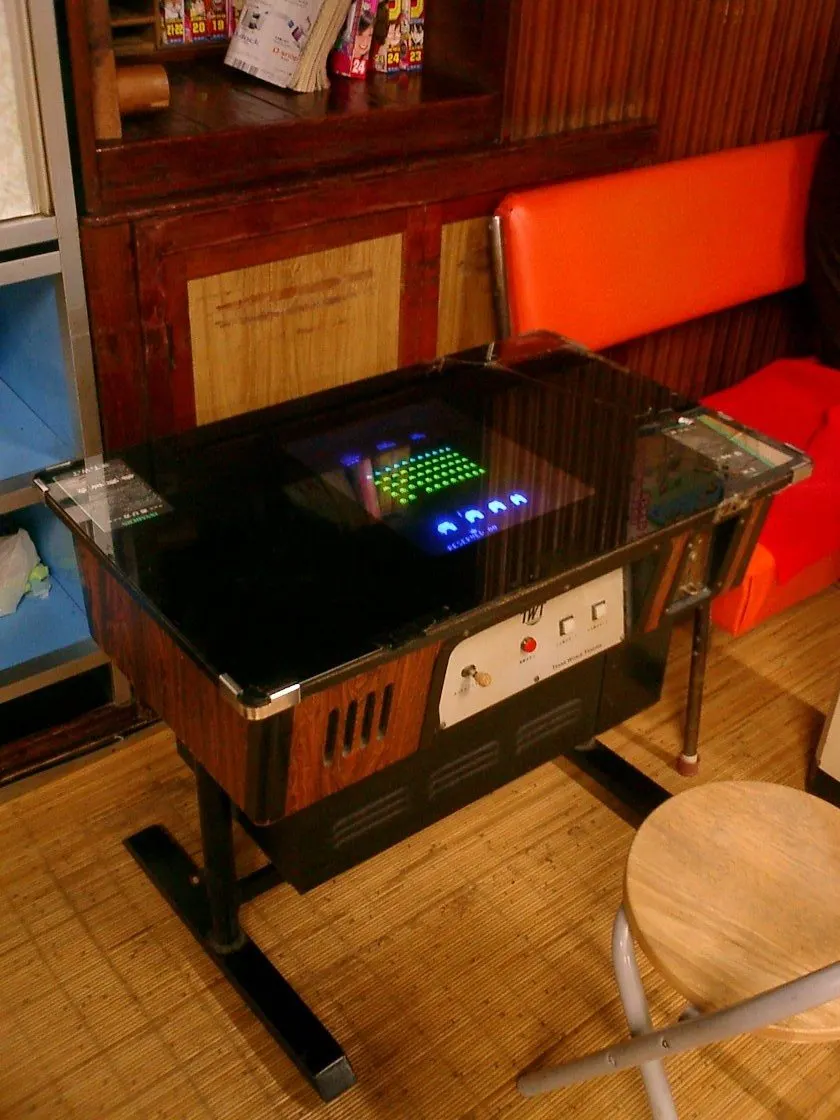 A 1978-style Space Invaders cocktail table cabinet with a glass top and a control panel at one end, in a cafe