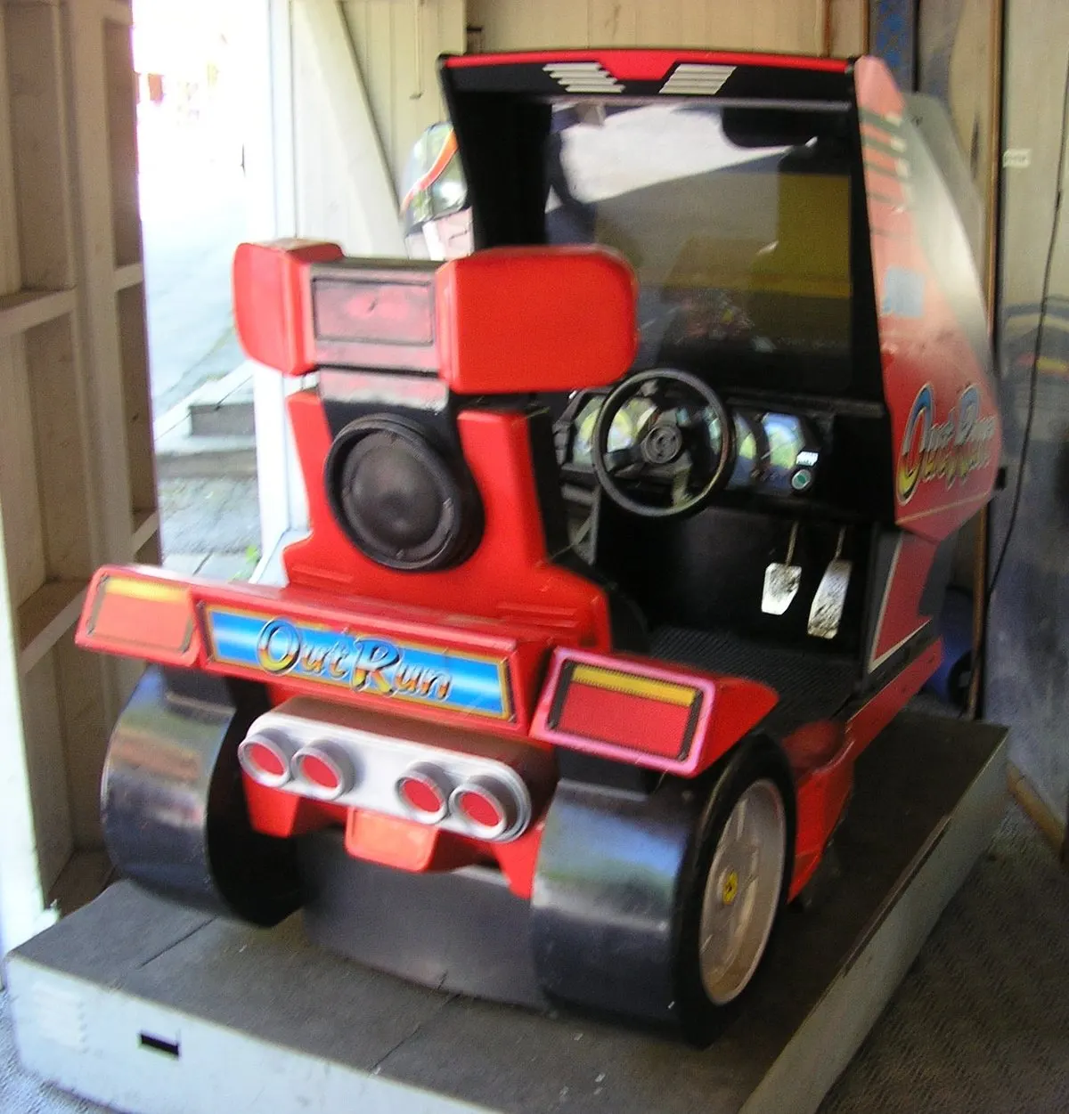 A red 1986 Out Run sit-down arcade cabinet shaped like a car, with a seat, wheel and pedals