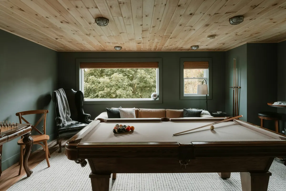 Pool table in the middle of a rec room with a wood ceiling, a sofa and windows along the walls