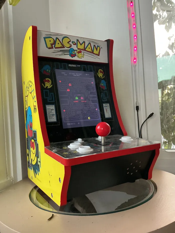 A small yellow and red joystick arcade machine on a round table, with a red-ball joystick and white buttons